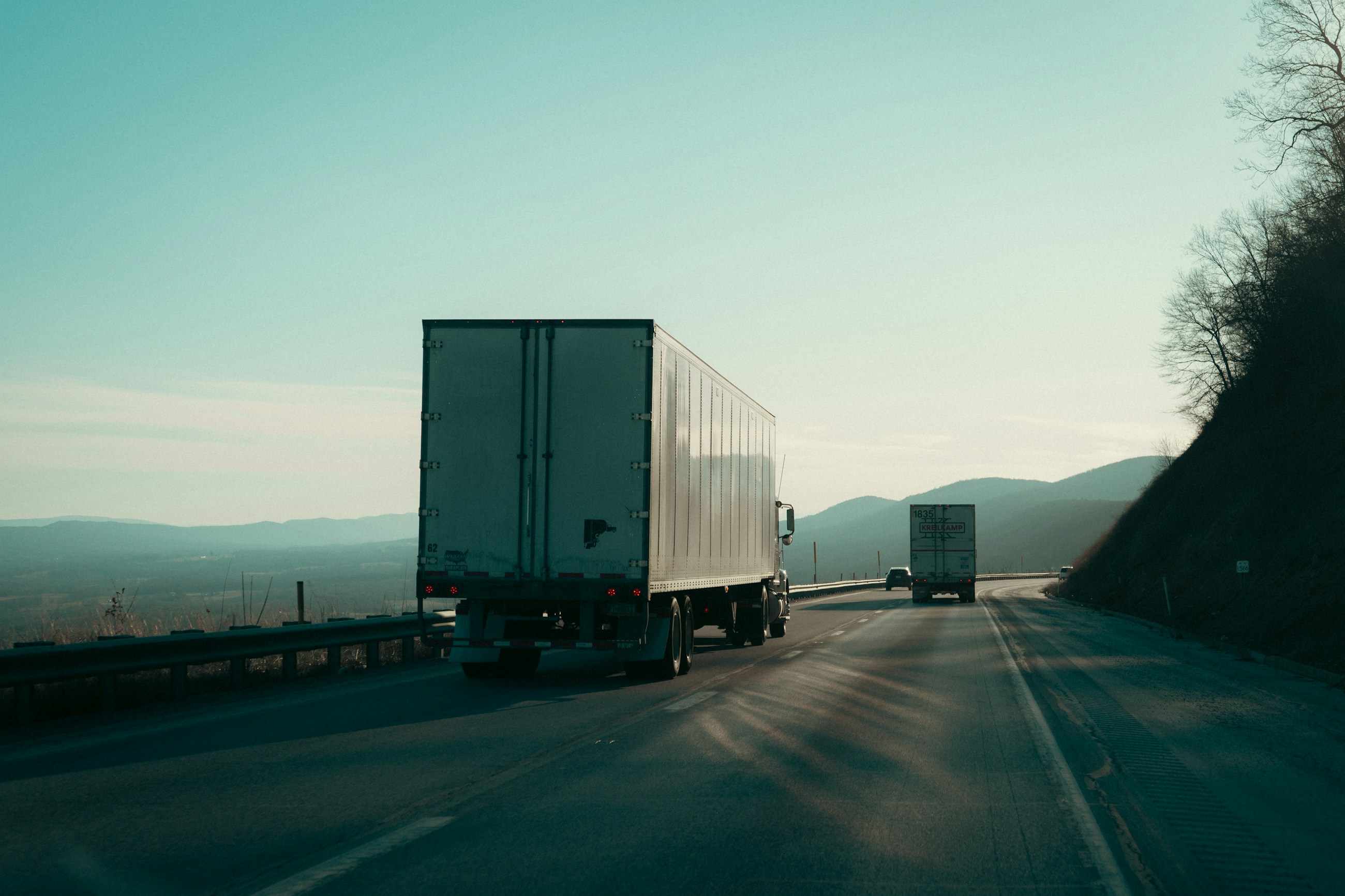 Two semi-trucks traveling on a wooded highway